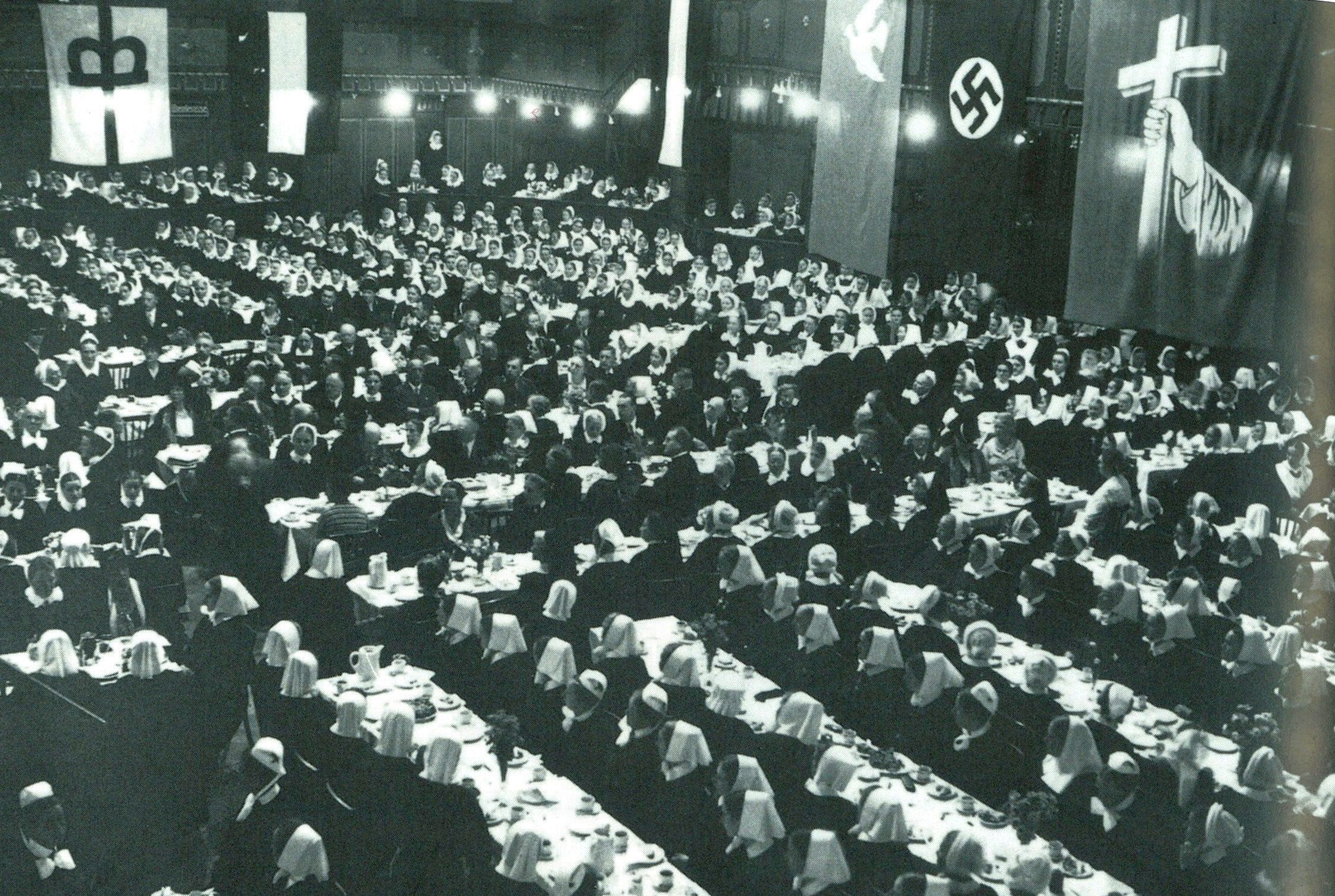 Viele Menschen sitzen an Tafeln in einem großen Saal